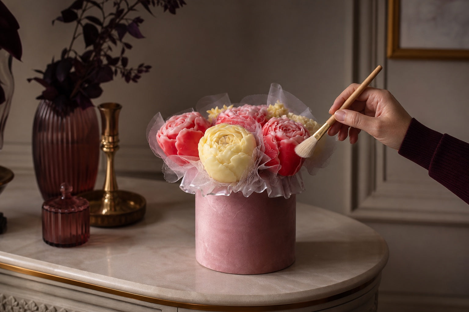 A hand gently dusting an unlit floral candle bouquet with a soft brush in a cool dry interior