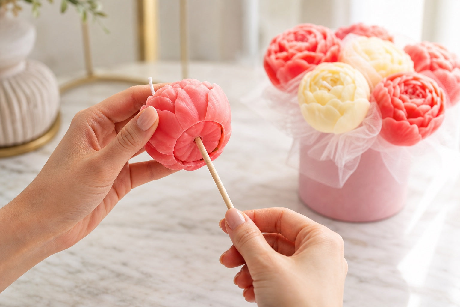 Two hands carefully pulling the wooden support straight out from the base of one coral wax flower candle