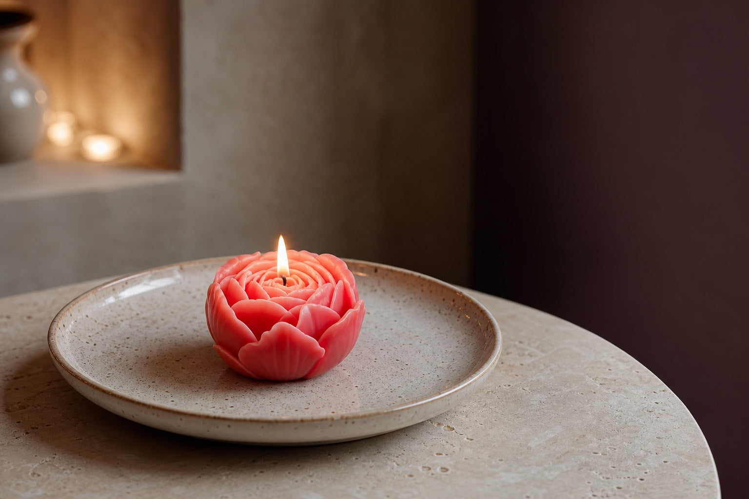 One coral wax flower candle burning by itself on a wide heat-resistant ceramic plate